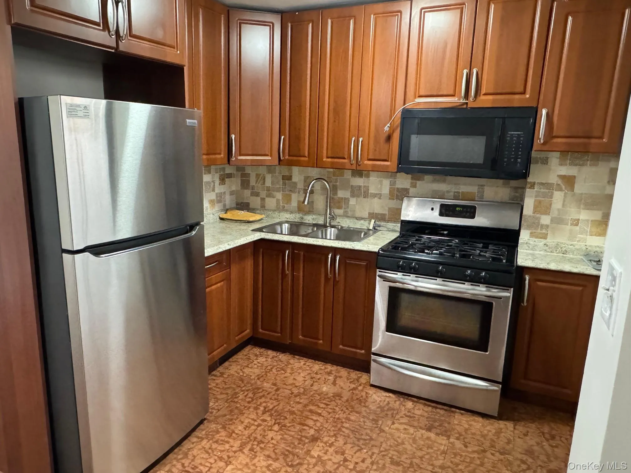 Kitchen featuring appliances with stainless steel finishes, decorative backsplash, brown cabinets, and light stone countertops Kitchen featuring appliances with stainless steel finishes, decorative backsplash, brown cabinets, and light stone countertops