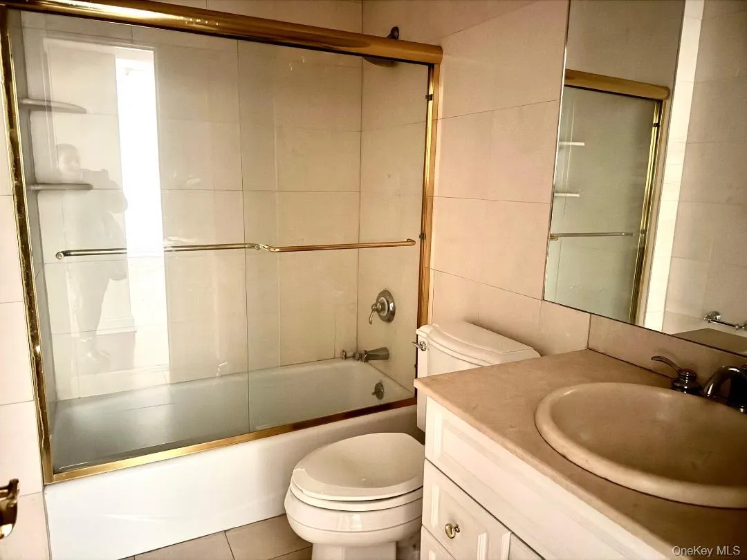 Full bath featuring vanity, bath / shower combo with glass door, tile walls, and tile patterned flooring Full bath featuring vanity, bath / shower combo with glass door, tile walls, and tile patterned flooring