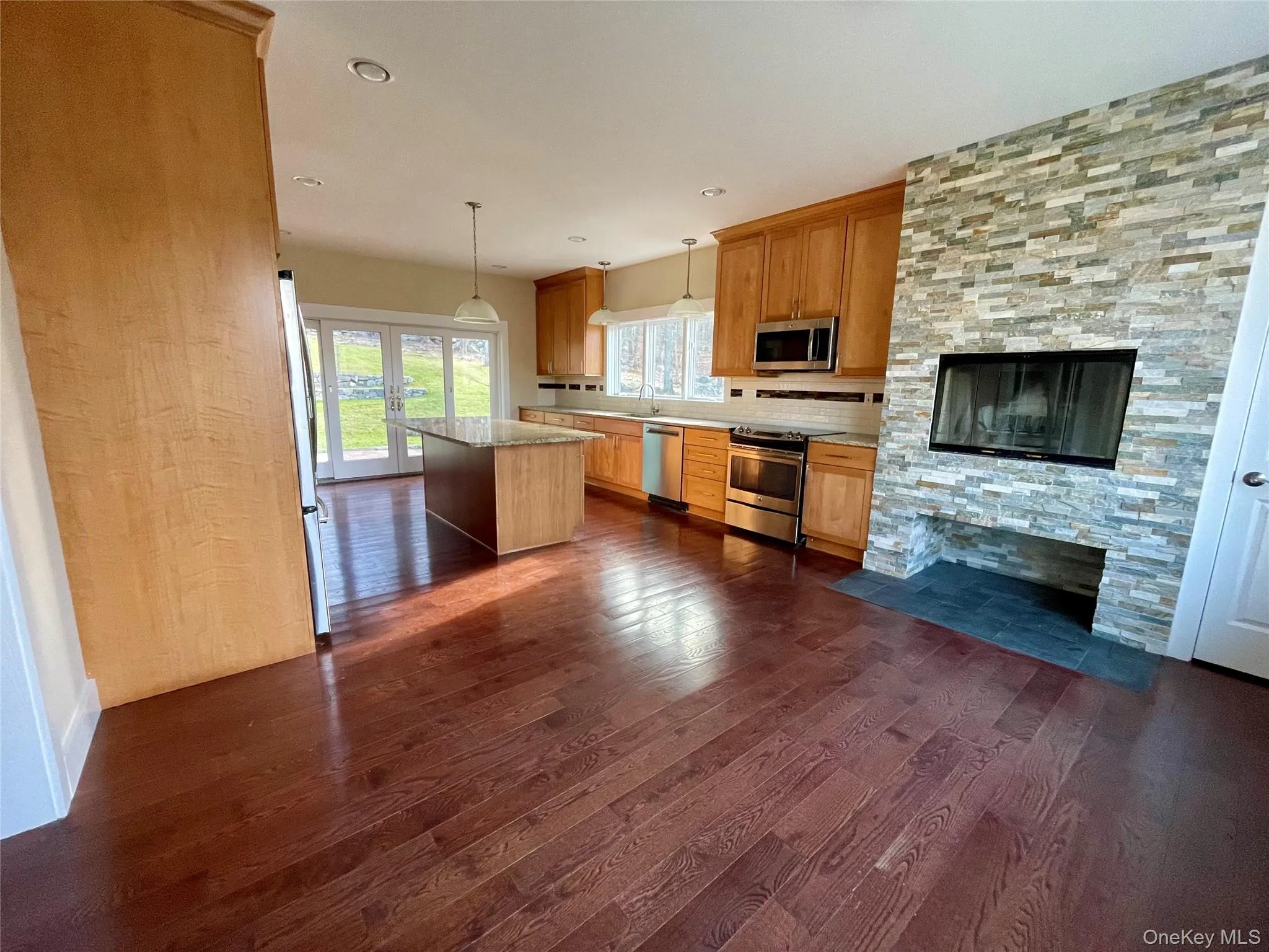 Kitchen with a fireplace, hanging light fixtures, appliances with stainless steel finishes, dark wood-type flooring, and french doors Kitchen with a fireplace, hanging light fixtures, appliances with stainless steel finishes, dark wood-type flooring, and french doors