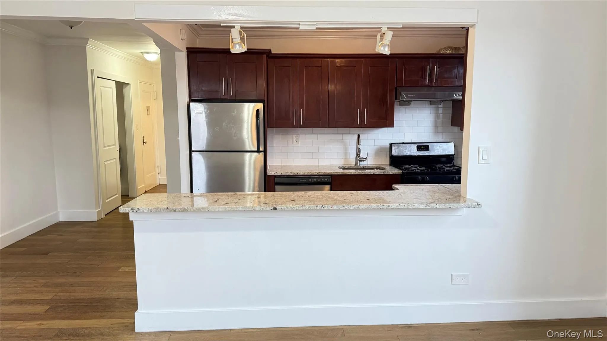 Kitchen featuring stainless steel appliances, tasteful backsplash, dark brown cabinetry, dark wood-type flooring, and ornamental molding Kitchen featuring stainless steel appliances, tasteful backsplash, dark brown cabinetry, dark wood-type flooring, and ornamental molding