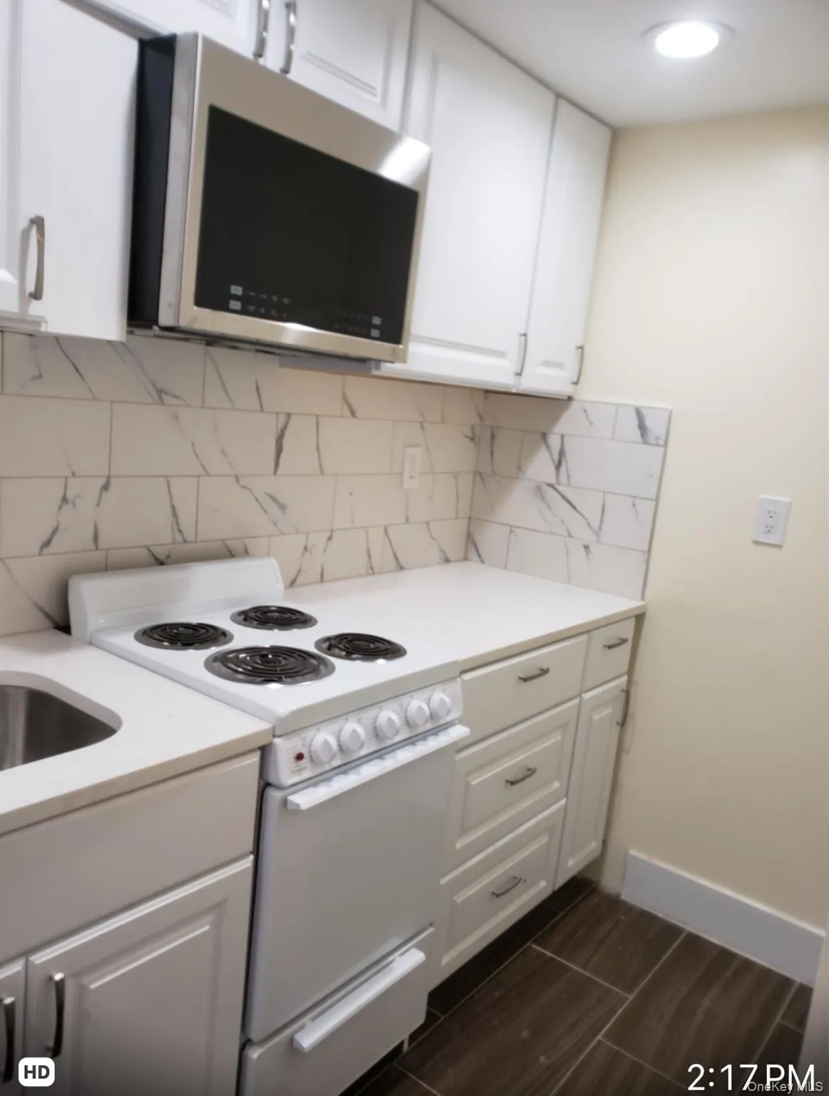 Kitchen with electric stove, stainless steel microwave, white cabinetry, and tasteful backsplash Kitchen with electric stove, stainless steel microwave, white cabinetry, and tasteful backsplash