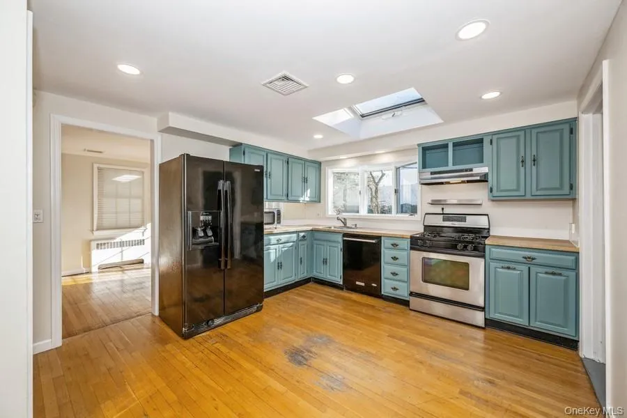 Kitchen featuring a skylight, black appliances, light wood-style floors, light countertops, and radiator Kitchen featuring a skylight, black appliances, light wood-style floors, light countertops, and radiator