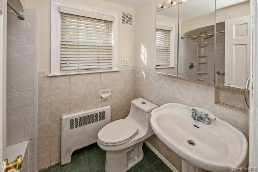 Full bath featuring radiator heating unit, dark tile patterned flooring, washtub / shower combination, and tile walls Full bath featuring radiator heating unit, dark tile patterned flooring, washtub / shower combination, and tile walls