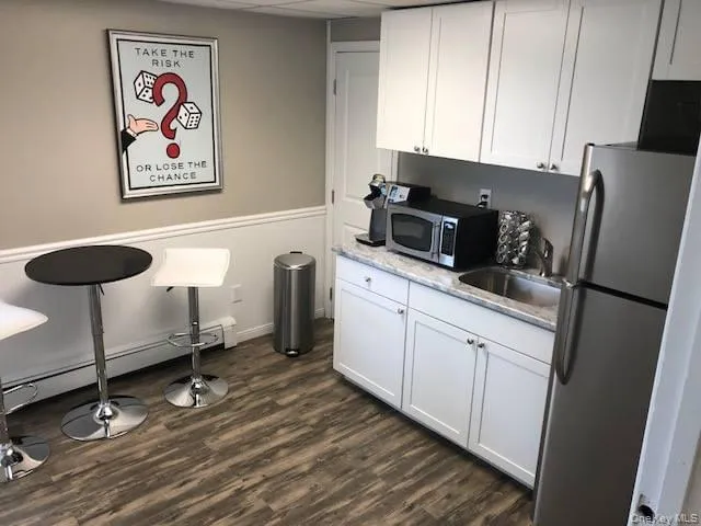 Kitchen featuring stainless steel appliances, a baseboard radiator, white cabinets, dark wood-style floors, and a wainscoted wall Kitchen featuring stainless steel appliances, a baseboard radiator, white cabinets, dark wood-style floors, and a wainscoted wall