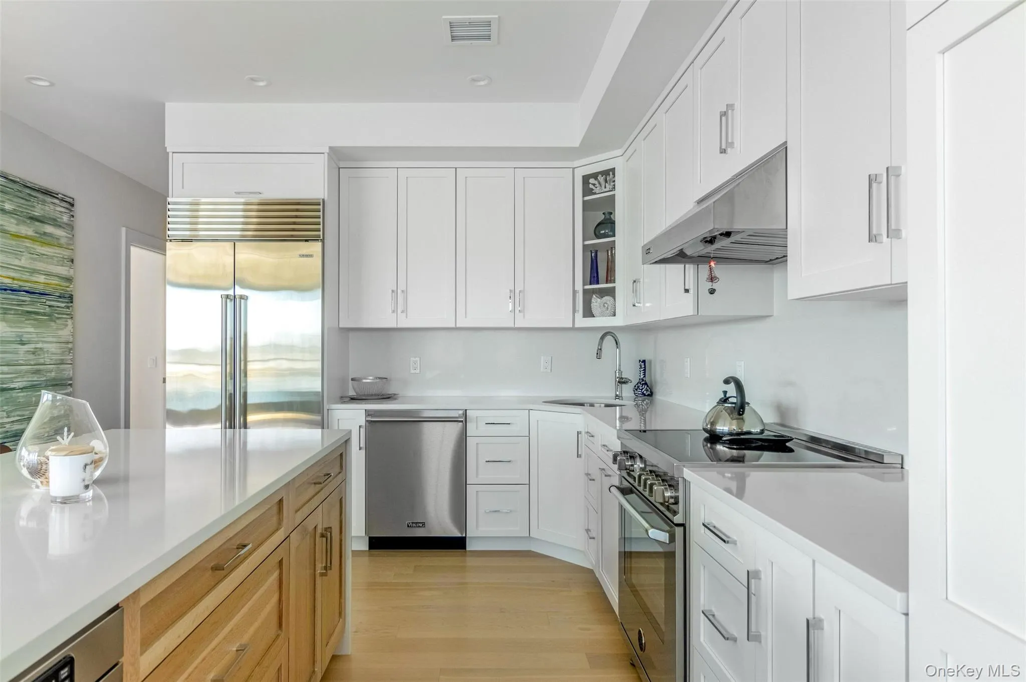 Kitchen with stainless steel appliances, white cabinets, light wood-style floors, under cabinet range hood, and glass insert cabinets Kitchen with stainless steel appliances, white cabinets, light wood-style floors, under cabinet range hood, and glass insert cabinets