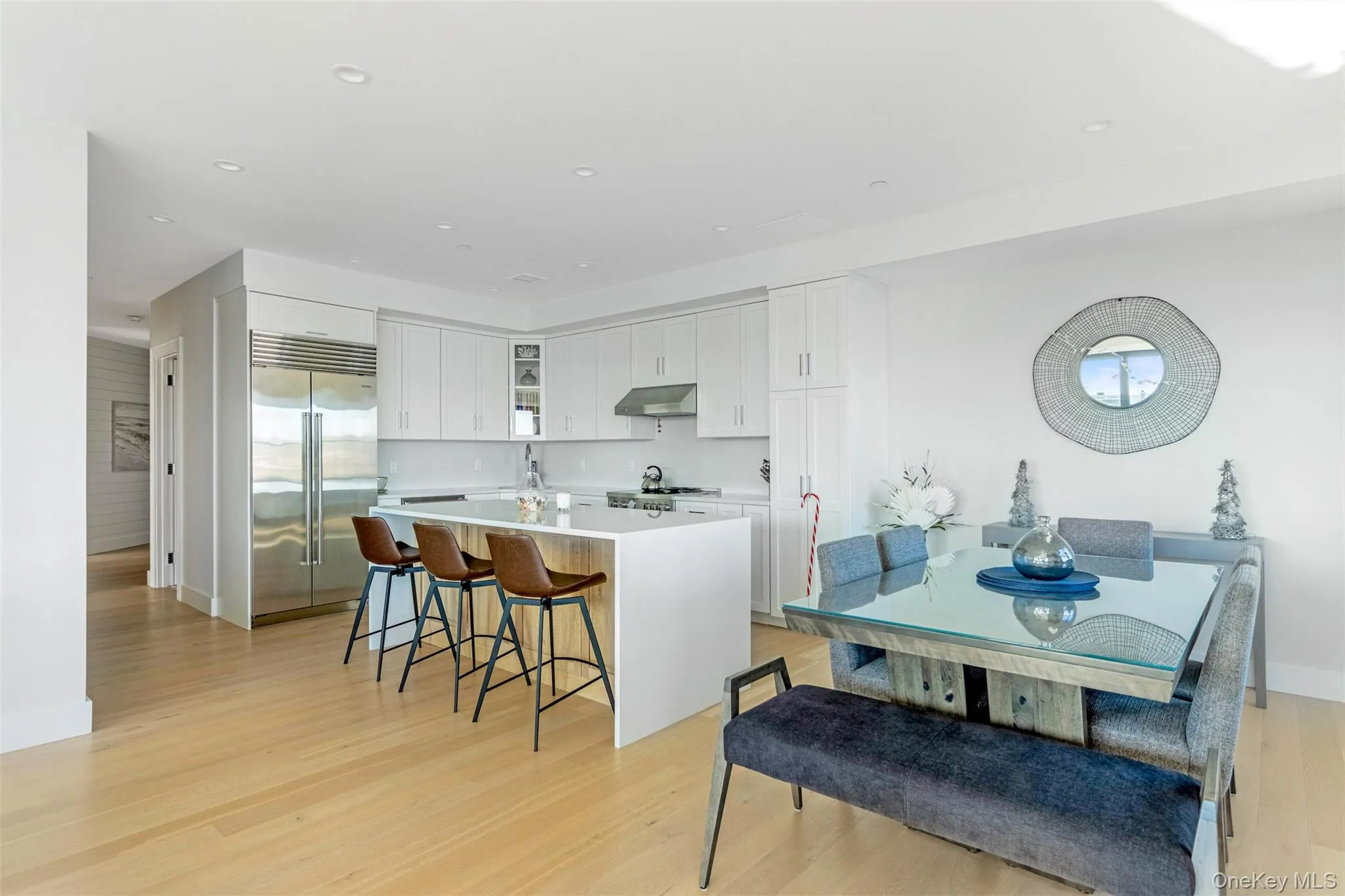 Kitchen featuring white cabinets, a center island with sink, stainless steel built in refrigerator, a breakfast bar, and recessed lighting Kitchen featuring white cabinets, a center island with sink, stainless steel built in refrigerator, a breakfast bar, and recessed lighting