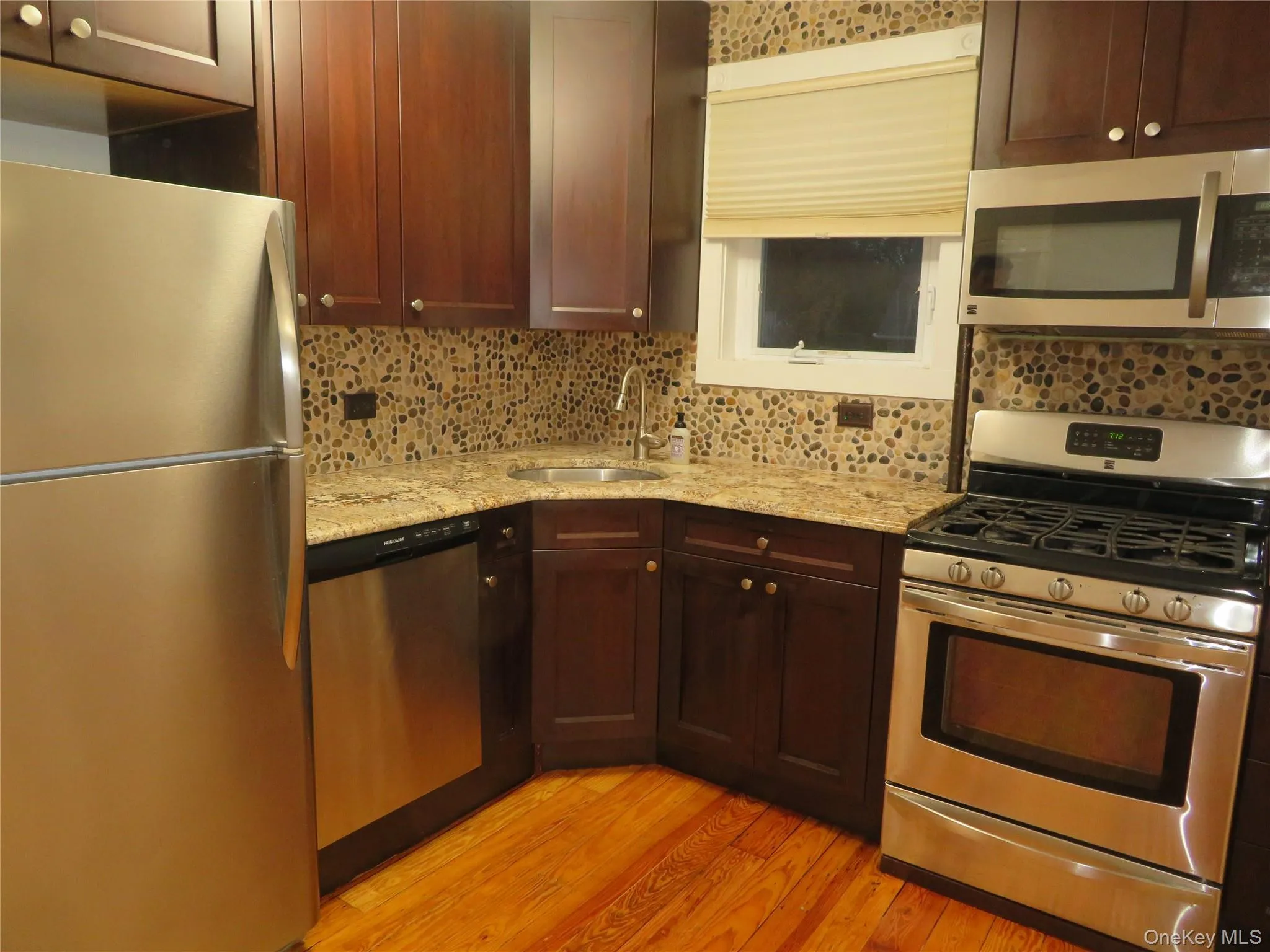 Kitchen with appliances with stainless steel finishes, light stone counters, tasteful backsplash, and light wood-type flooring Kitchen with appliances with stainless steel finishes, light stone counters, tasteful backsplash, and light wood-type flooring