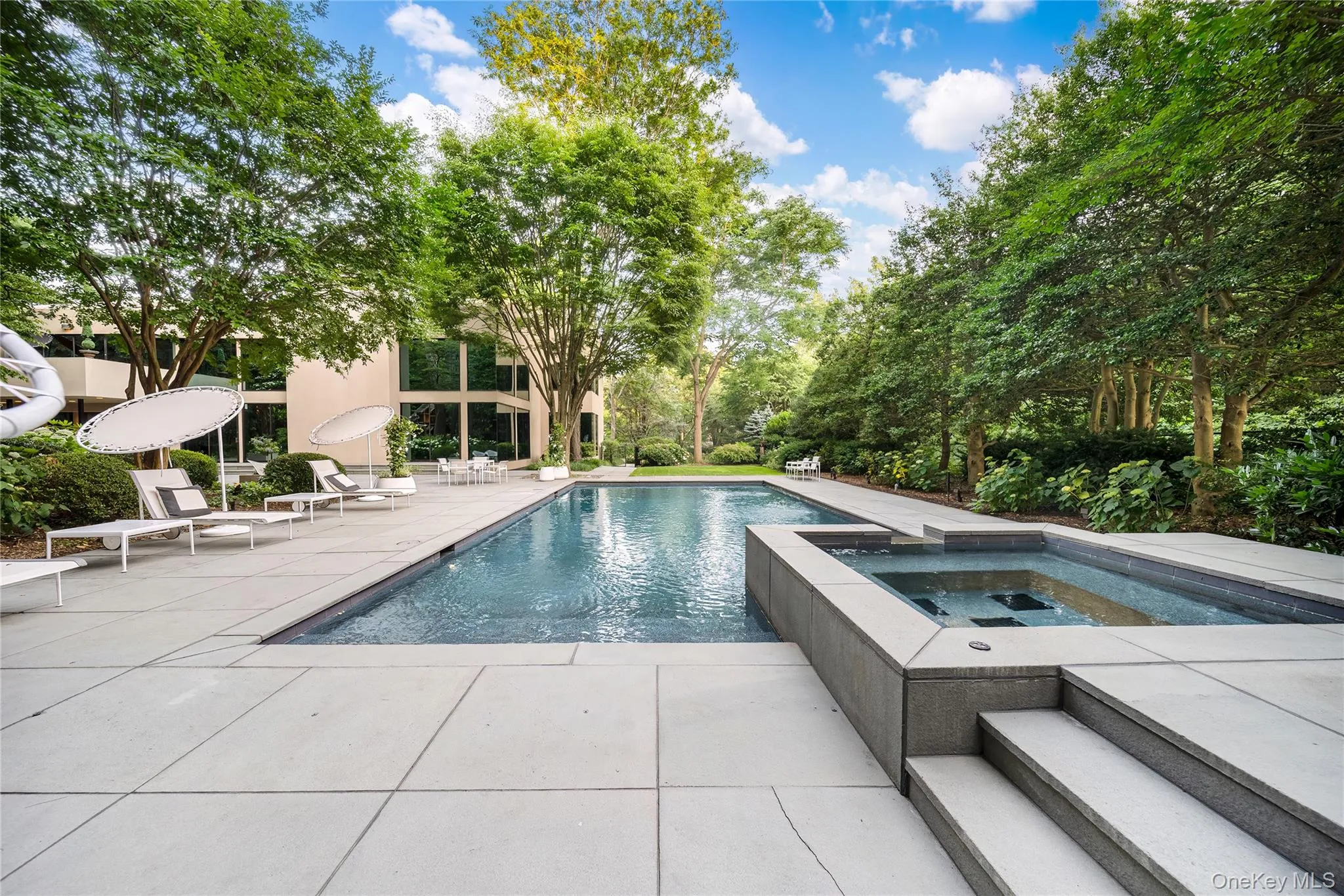 View of pool featuring a patio area, view of scattered trees, and a pool with connected hot tub View of pool featuring a patio area, view of scattered trees, and a pool with connected hot tub