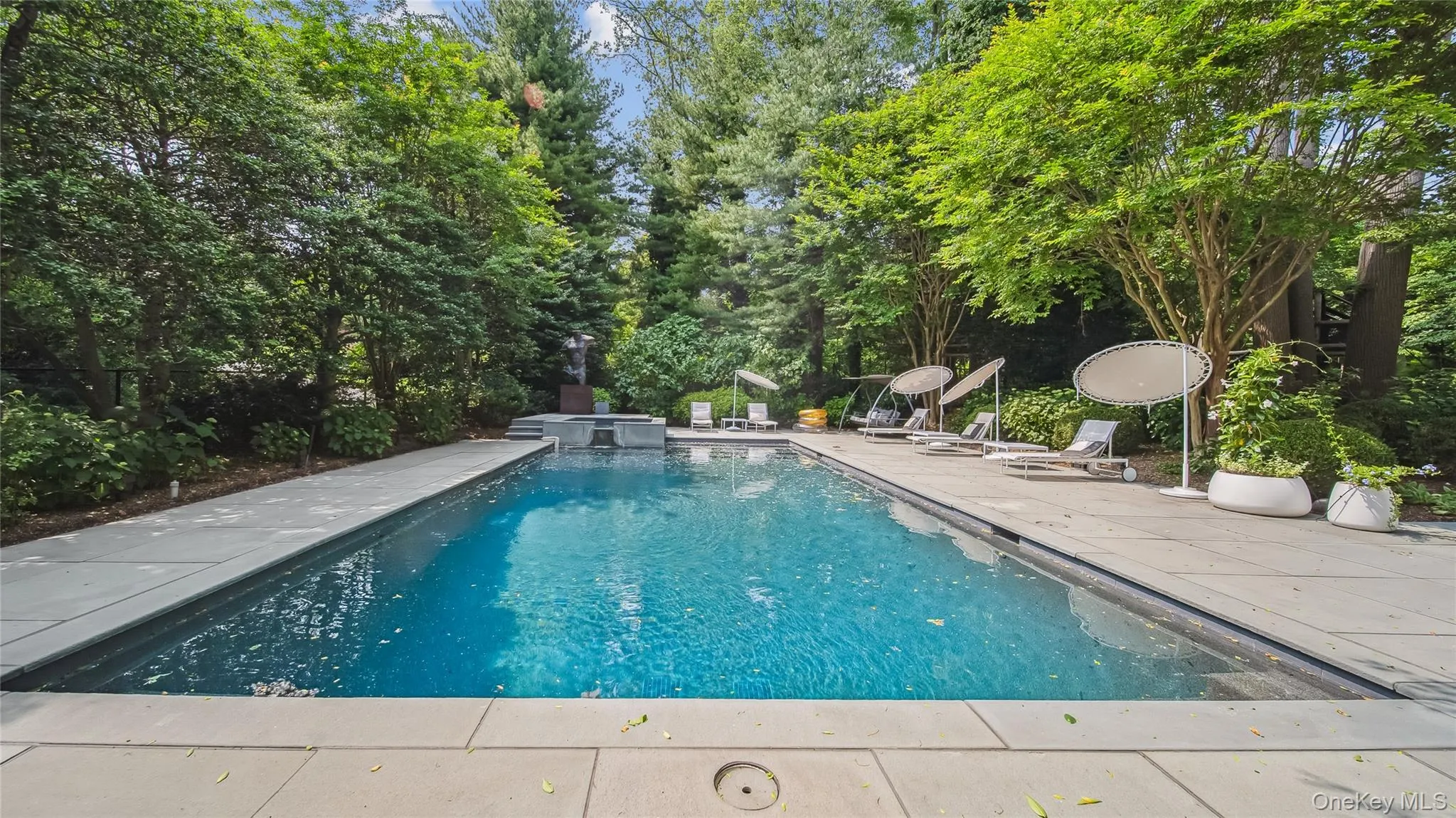 View of swimming pool featuring a patio area, a pool with connected hot tub, and view of scattered trees View of swimming pool featuring a patio area, a pool with connected hot tub, and view of scattered trees