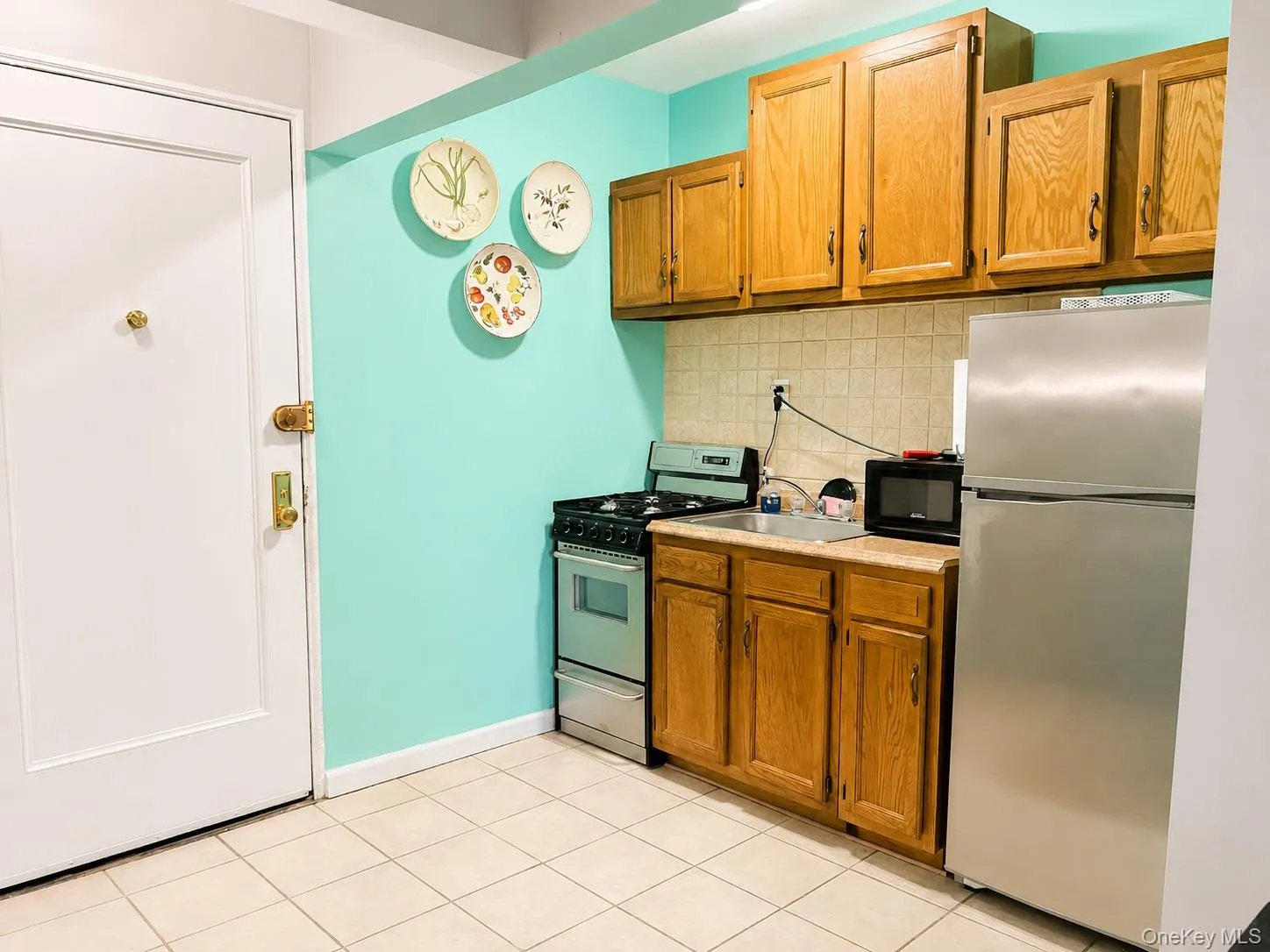 Kitchen with stainless appliances backsplash, light countertops, and brown cabinetry Kitchen with stainless appliances backsplash, light countertops, and brown cabinetry