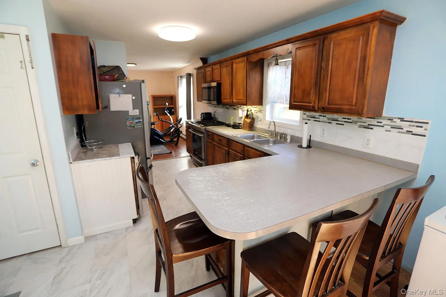 Kitchen featuring a kitchen bar, light countertops, a peninsula, and appliances with stainless steel finishes Kitchen featuring a kitchen bar, light countertops, a peninsula, and appliances with stainless steel finishes