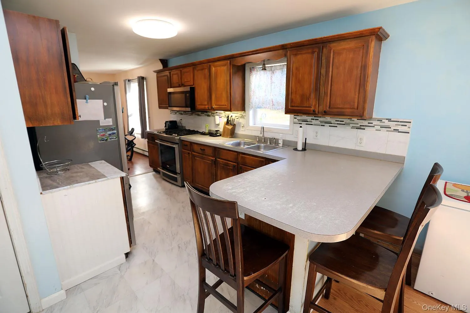 Kitchen with a kitchen bar, light countertops, a peninsula, appliances with stainless steel finishes, and tasteful backsplash Kitchen with a kitchen bar, light countertops, a peninsula, appliances with stainless steel finishes, and tasteful backsplash