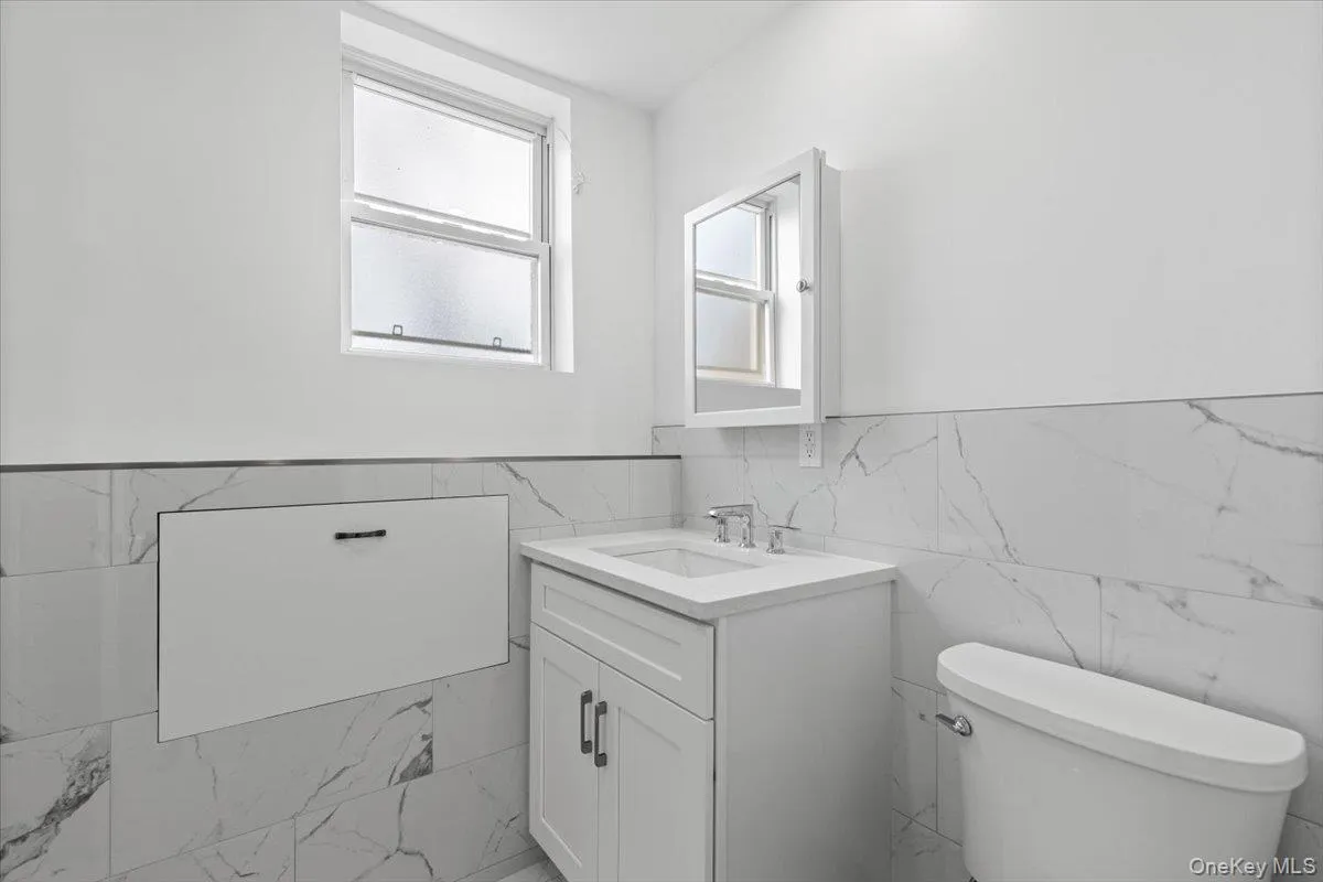Half bath featuring vanity, healthy amount of natural light, tile walls, and wainscoting Half bath featuring vanity, healthy amount of natural light, tile walls, and wainscoting
