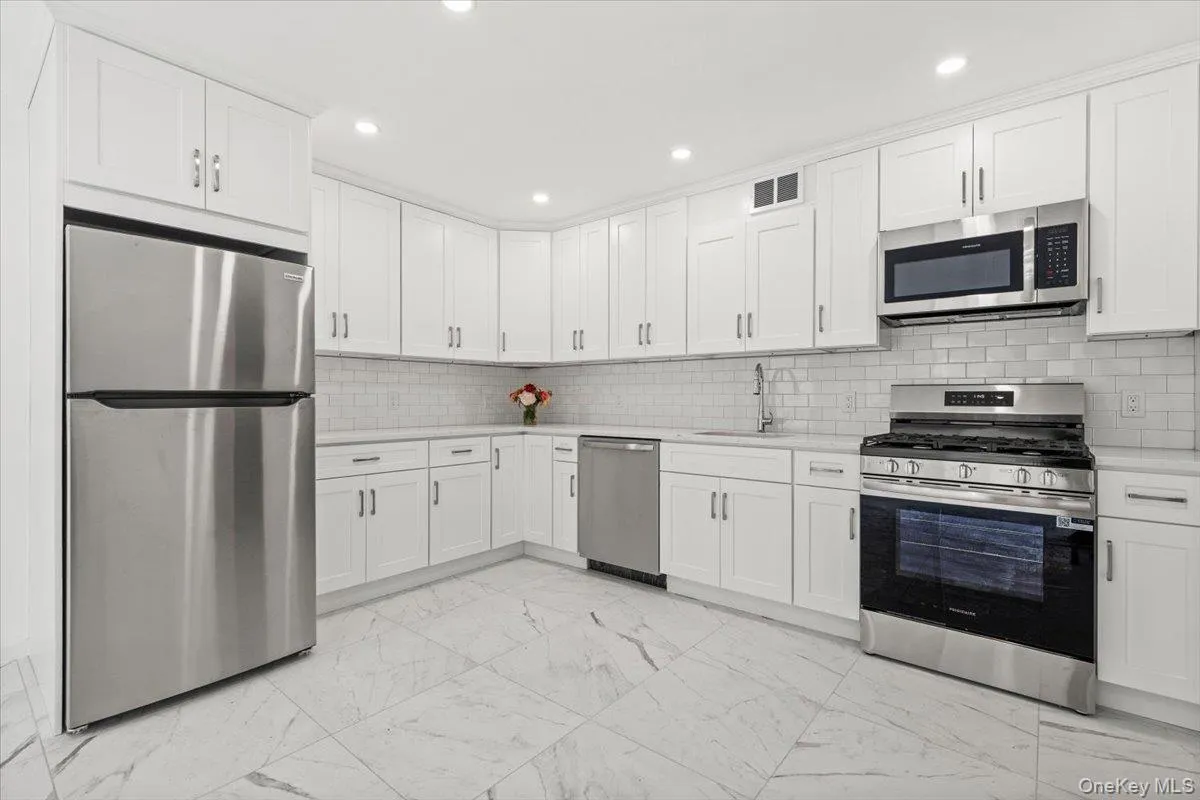 Kitchen with appliances with stainless steel finishes, light marble finish floors, backsplash, white cabinetry, and recessed lighting Kitchen with appliances with stainless steel finishes, light marble finish floors, backsplash, white cabinetry, and recessed lighting