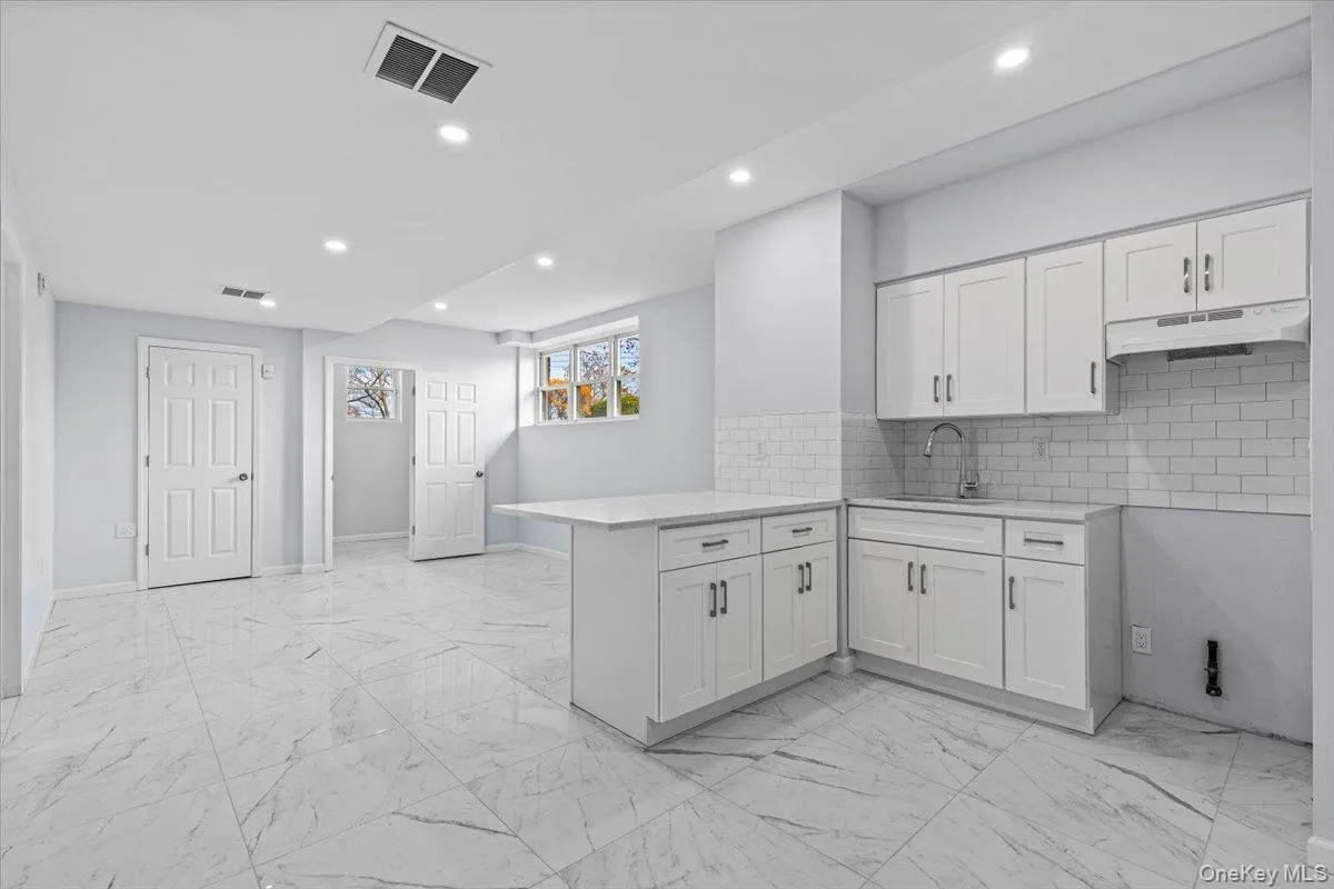 Kitchen featuring tasteful backsplash, a peninsula, light marble finish flooring, white cabinetry, and recessed lighting Kitchen featuring tasteful backsplash, a peninsula, light marble finish flooring, white cabinetry, and recessed lighting