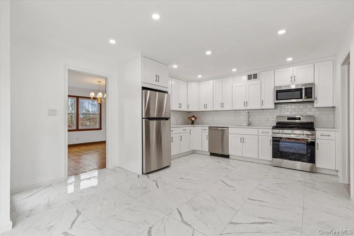 Kitchen with light marble finish floors, appliances with stainless steel finishes, a chandelier, tasteful backsplash, and recessed lighting Kitchen with light marble finish floors, appliances with stainless steel finishes, a chandelier, tasteful backsplash, and recessed lighting