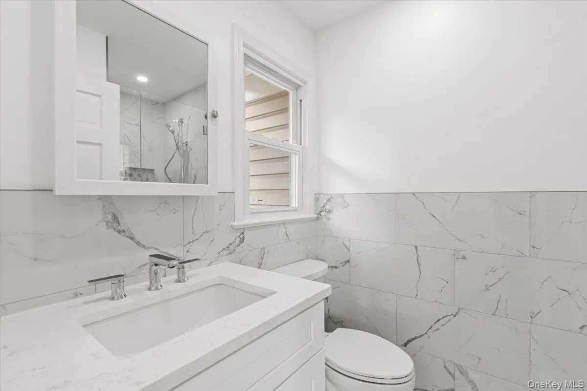 Full bathroom with a marble finish shower, vanity, and tile walls Full bathroom with a marble finish shower, vanity, and tile walls