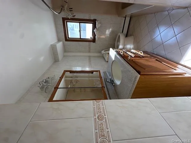 Bathroom featuring tile walls, light tile patterned floors, vanity, shower / bathtub combination, and baseboard heating Bathroom featuring tile walls, light tile patterned floors, vanity, shower / bathtub combination, and baseboard heating