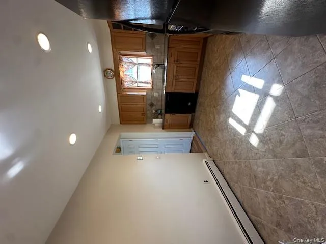 Kitchen with baseboard heating, refrigerator, brown cabinets, backsplash, and recessed lighting Kitchen with baseboard heating, refrigerator, brown cabinets, backsplash, and recessed lighting