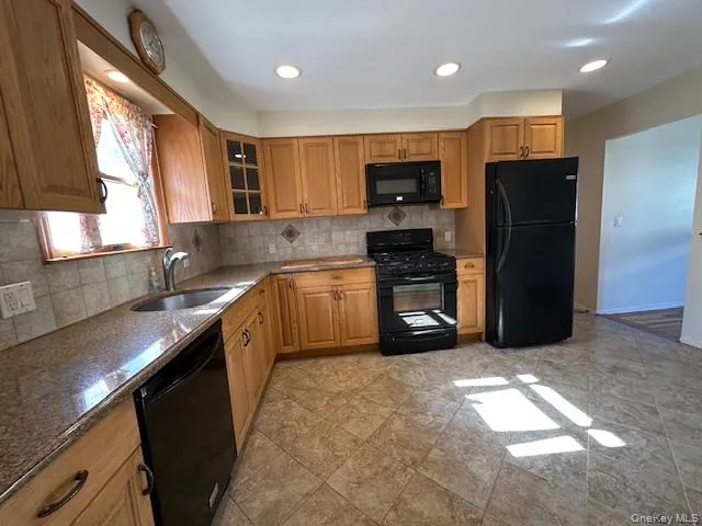 Kitchen featuring tasteful backsplash, black appliances, dark stone countertops, glass insert cabinets, and recessed lighting Kitchen featuring tasteful backsplash, black appliances, dark stone countertops, glass insert cabinets, and recessed lighting