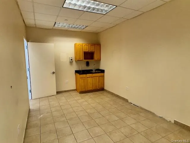 Kitchen featuring dark countertops, a paneled ceiling, brown cabinetry, and light tile patterned floors Kitchen featuring dark countertops, a paneled ceiling, brown cabinetry, and light tile patterned floors