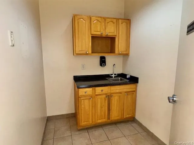 Bar area featuring dark countertops, light tile patterned floors, and brown cabinetry Bar area featuring dark countertops, light tile patterned floors, and brown cabinetry