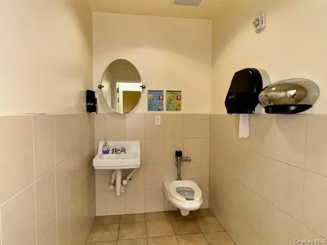 Half bath featuring tile patterned floors, tile walls, and a wainscoted wall Half bath featuring tile patterned floors, tile walls, and a wainscoted wall