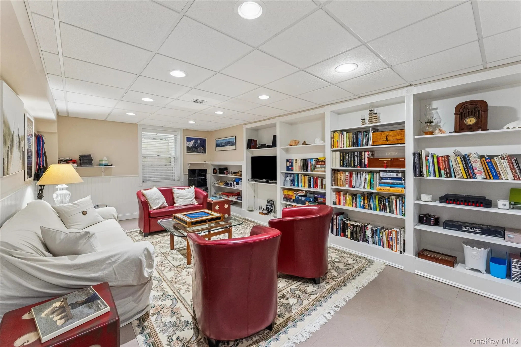 Living area featuring wainscoting, built in shelves, a paneled ceiling, and recessed lighting Living area featuring wainscoting, built in shelves, a paneled ceiling, and recessed lighting