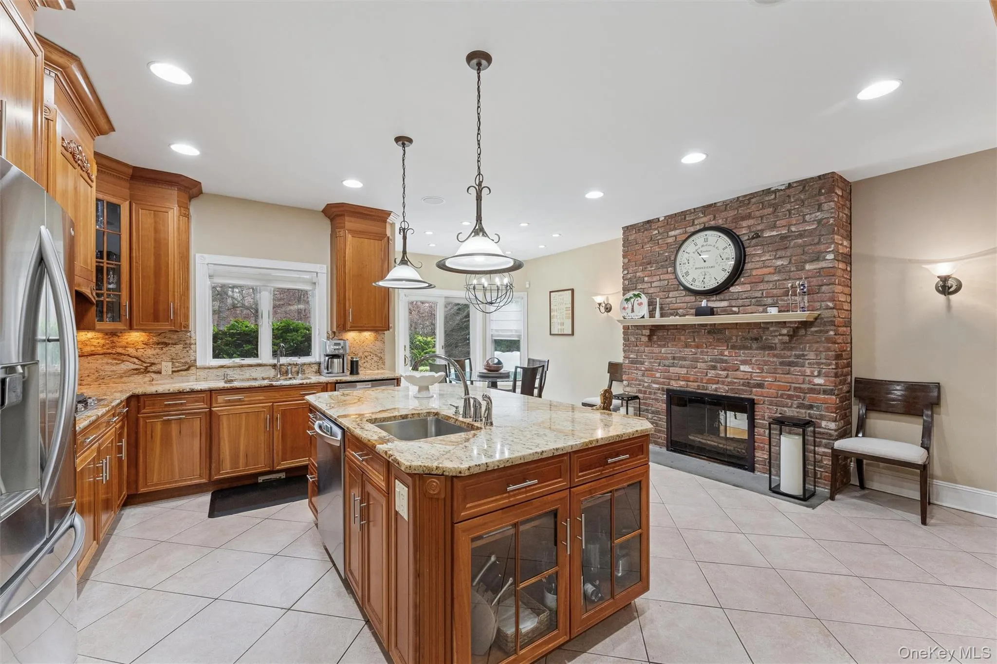 Kitchen featuring glass insert cabinets, brown cabinetry, pendant lighting, light stone countertops, and recessed lighting Kitchen featuring glass insert cabinets, brown cabinetry, pendant lighting, light stone countertops, and recessed lighting
