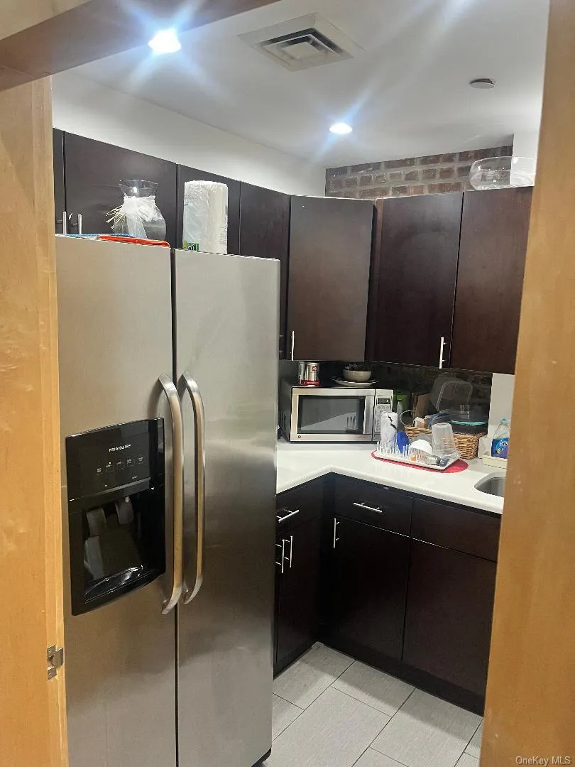 Kitchen featuring appliances with stainless steel finishes, light countertops, light tile patterned flooring, and dark brown cabinetry Kitchen featuring appliances with stainless steel finishes, light countertops, light tile patterned flooring, and dark brown cabinetry