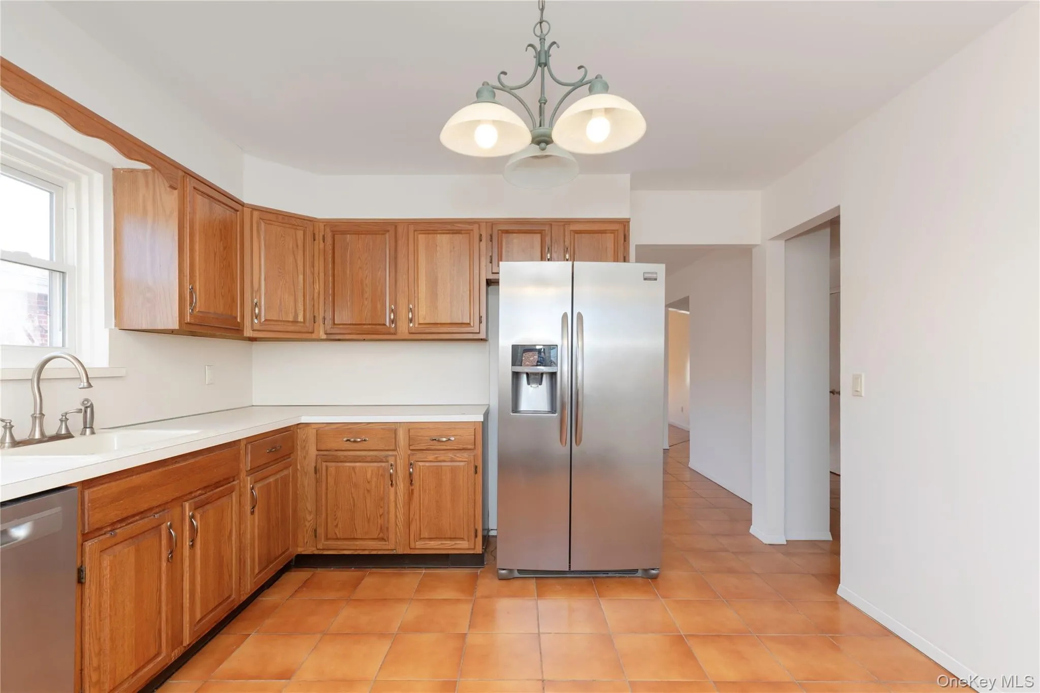 Kitchen featuring appliances with stainless steel finishes, light countertops, brown cabinets, pendant lighting, and light tile patterned flooring Kitchen featuring appliances with stainless steel finishes, light countertops, brown cabinets, pendant lighting, and light tile patterned flooring