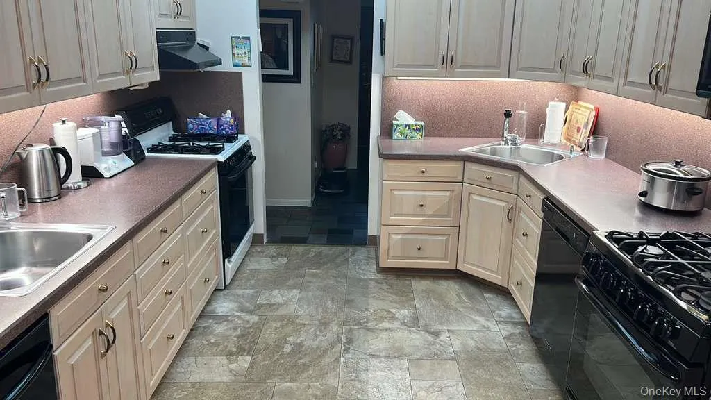 Kitchen with black appliances, under cabinet range hood, stone finish flooring, and light countertops Kitchen with black appliances, under cabinet range hood, stone finish flooring, and light countertops