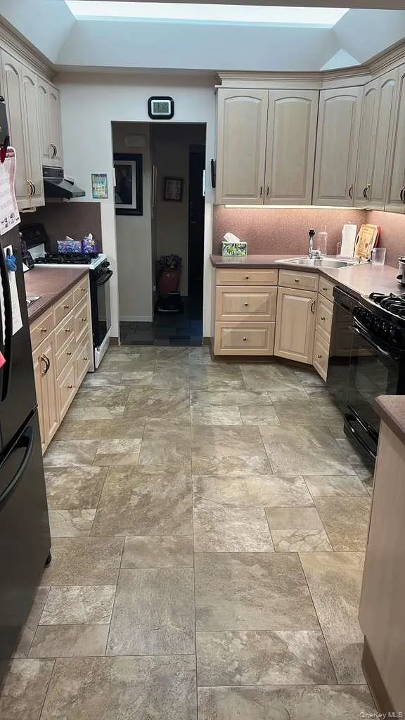 Kitchen featuring black appliances, stone finish floors, extractor fan, and tasteful backsplash Kitchen featuring black appliances, stone finish floors, extractor fan, and tasteful backsplash