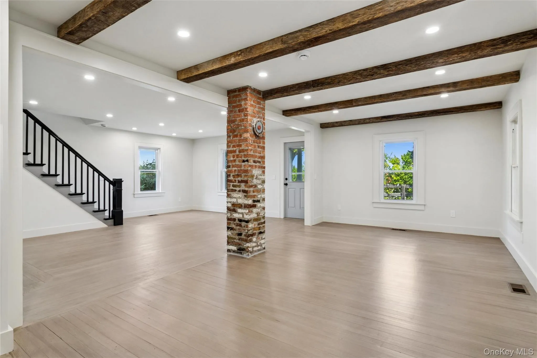 Unfurnished living room featuring light wood-style floors, beam ceiling, stairway, and recessed lighting Unfurnished living room featuring light wood-style floors, beam ceiling, stairway, and recessed lighting
