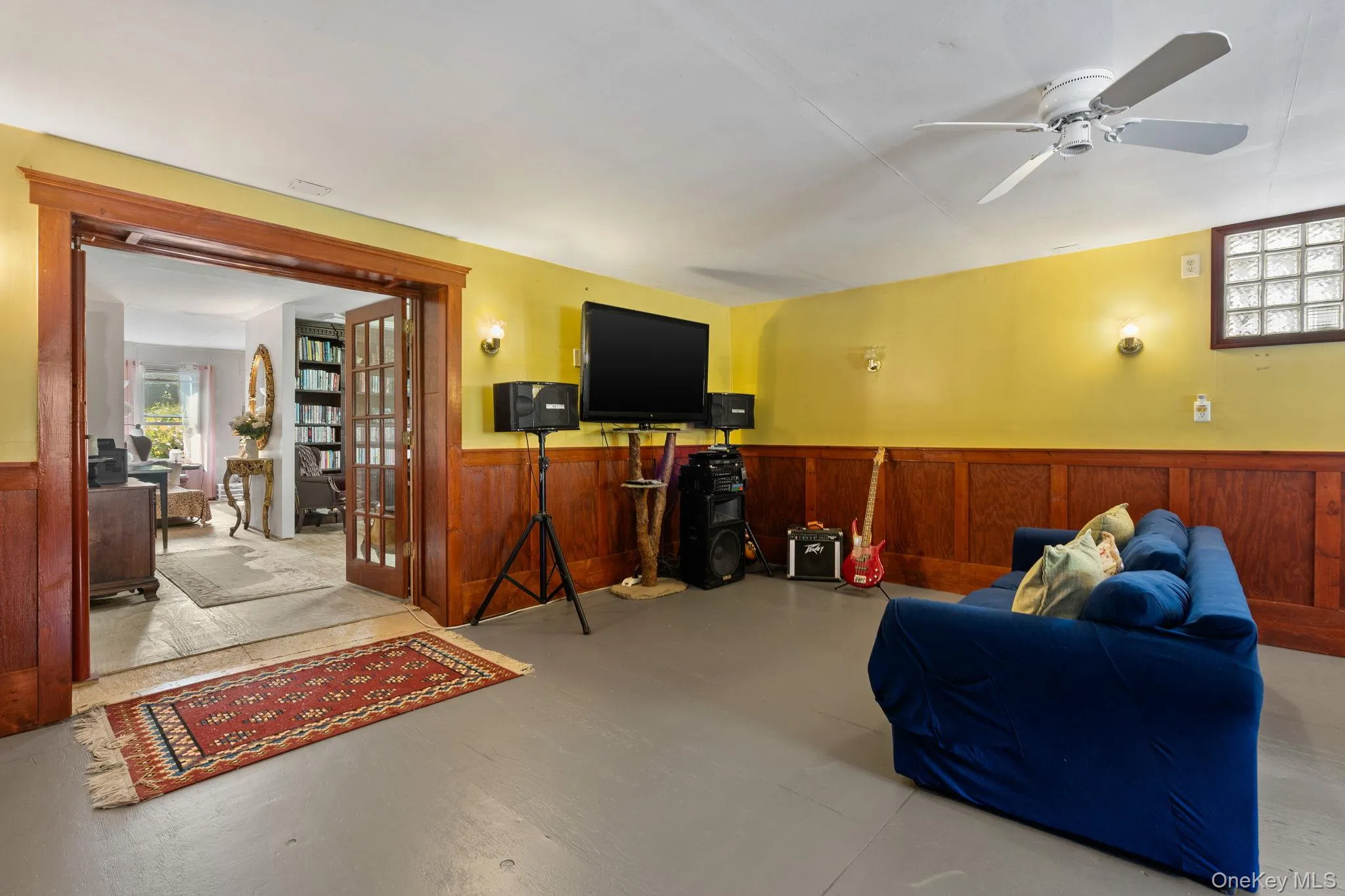 Living area featuring healthy amount of natural light, wainscoting, finished concrete flooring, ceiling fan, and a desk Living area featuring healthy amount of natural light, wainscoting, finished concrete flooring, ceiling fan, and a desk