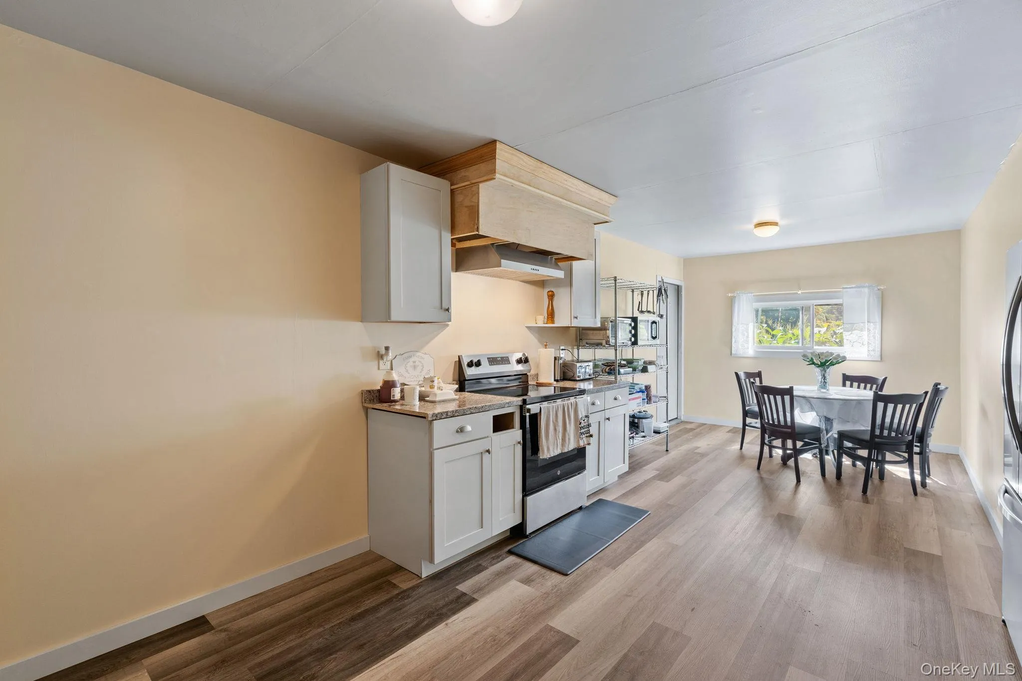 Kitchen featuring stainless steel electric stove, white cabinetry, light wood-type flooring, dark stone countertops, and exhaust hood Kitchen featuring stainless steel electric stove, white cabinetry, light wood-type flooring, dark stone countertops, and exhaust hood