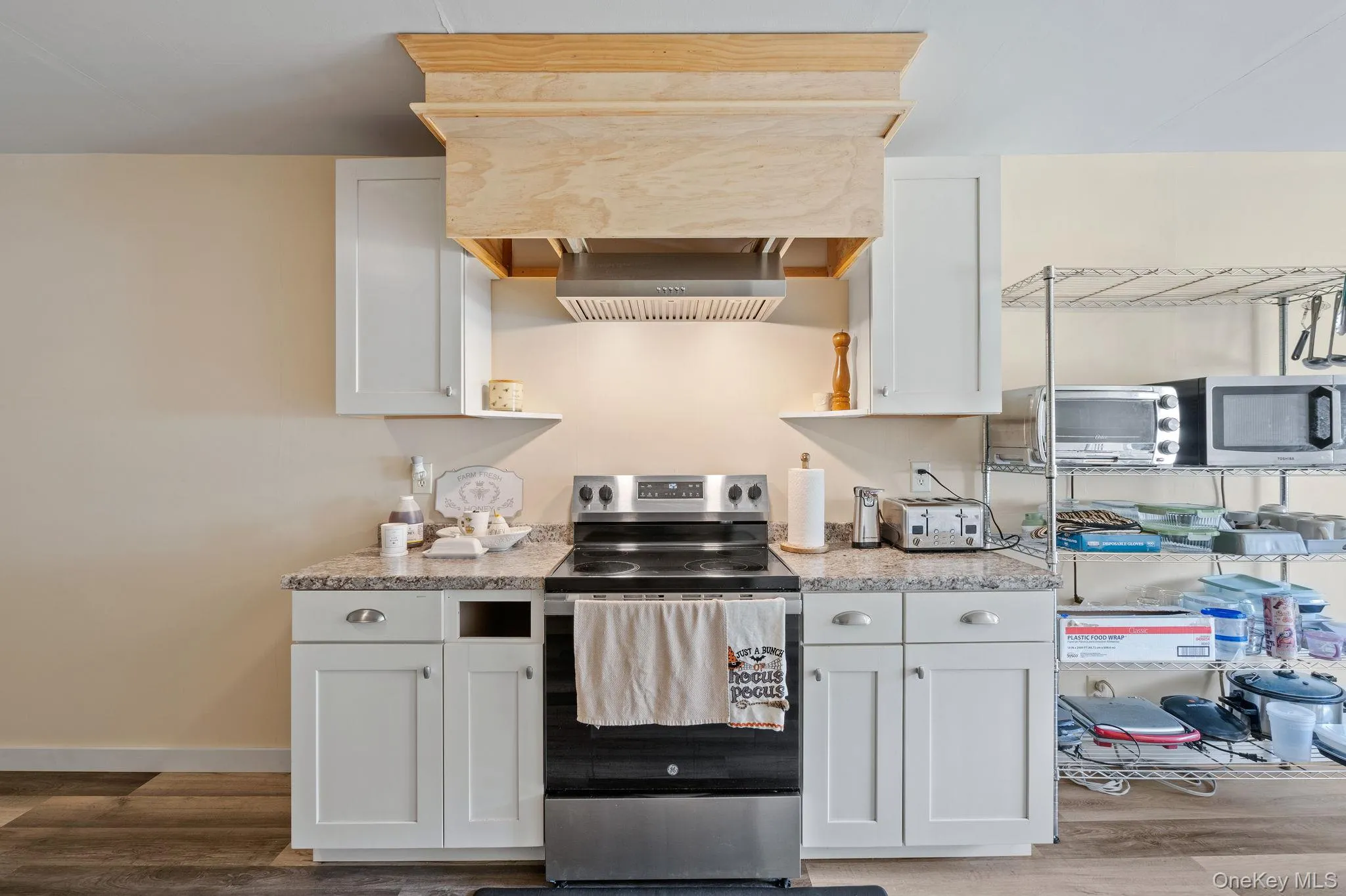 Kitchen with stainless steel appliances, white cabinetry, light wood-type flooring, ventilation hood, and light stone countertops Kitchen with stainless steel appliances, white cabinetry, light wood-type flooring, ventilation hood, and light stone countertops