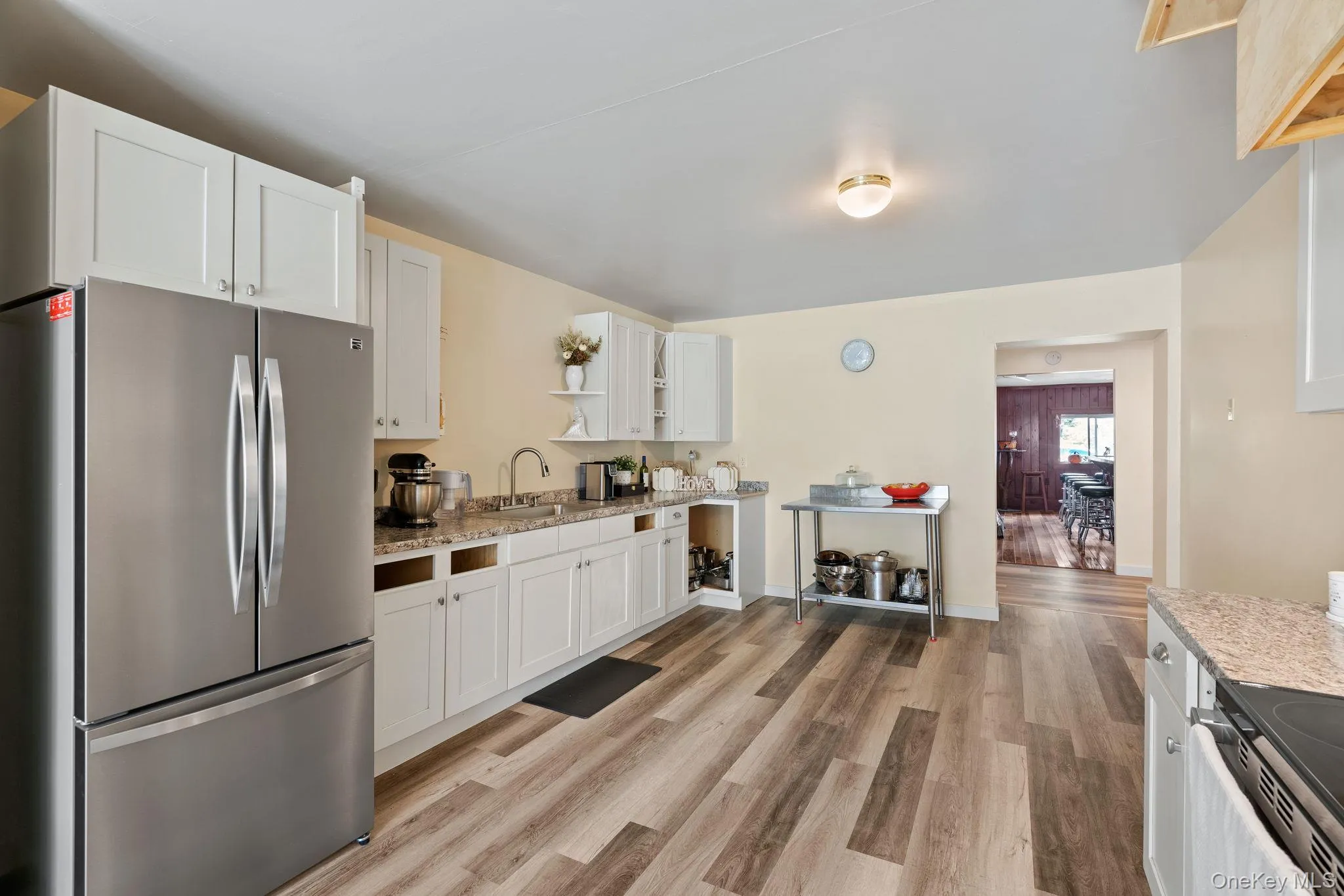 Kitchen featuring stainless steel appliances, open shelves, white cabinets, light stone counters, and light wood-style floors Kitchen featuring stainless steel appliances, open shelves, white cabinets, light stone counters, and light wood-style floors