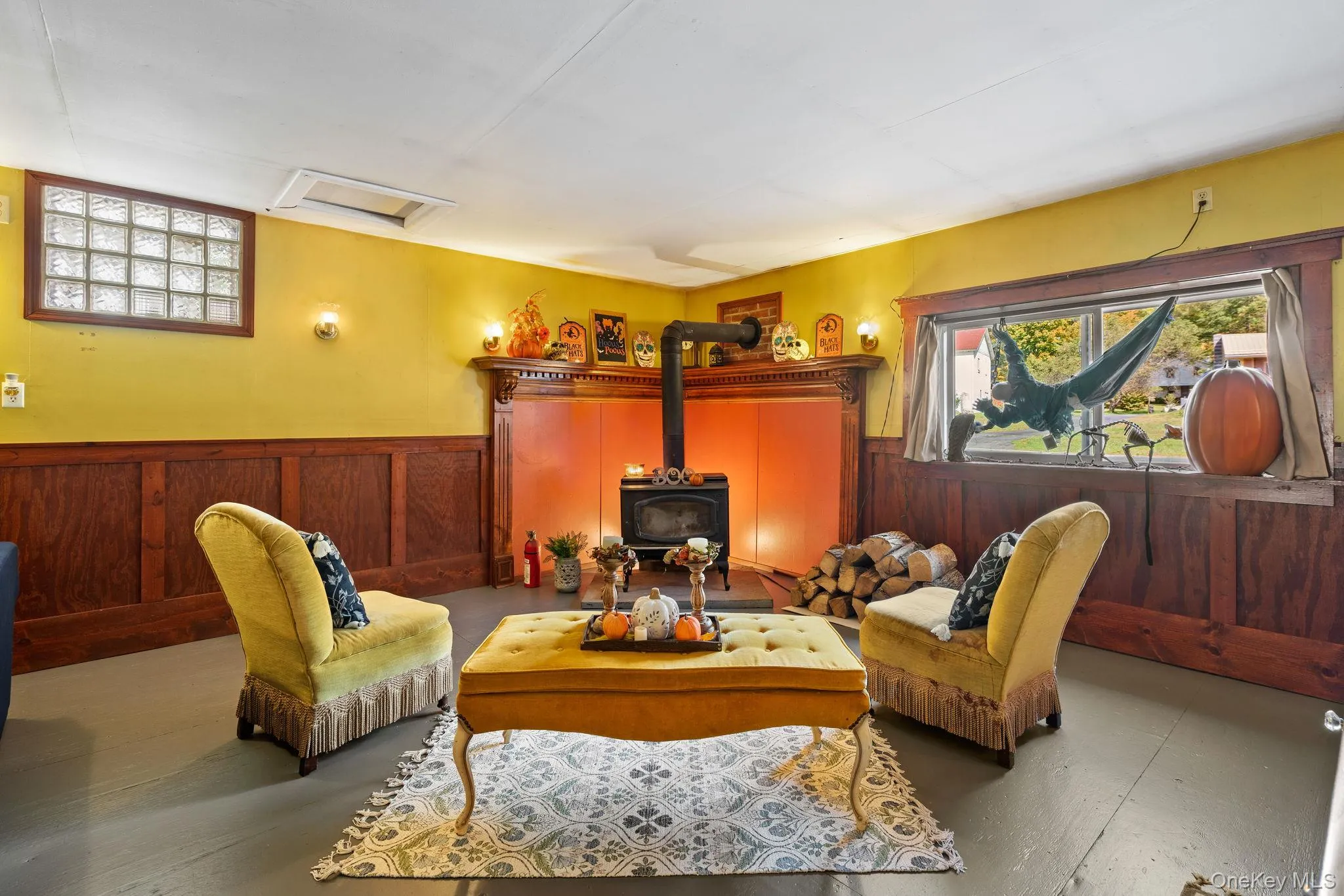 Living area with healthy amount of natural light, a wood stove, wainscoting, wood walls, and attic access Living area with healthy amount of natural light, a wood stove, wainscoting, wood walls, and attic access