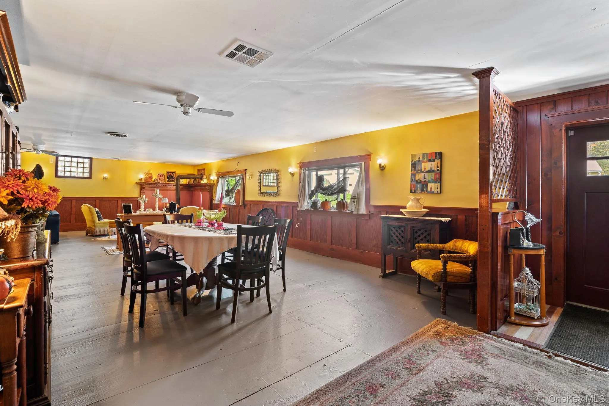 Dining room featuring wooden walls, a wainscoted wall, a ceiling fan, and concrete flooring Dining room featuring wooden walls, a wainscoted wall, a ceiling fan, and concrete flooring