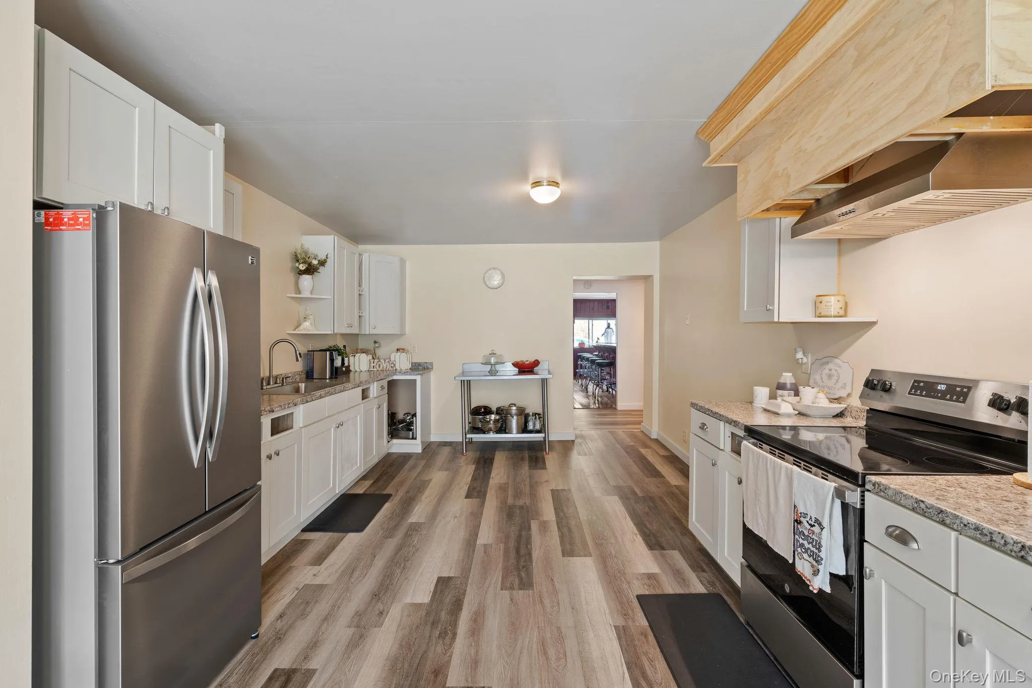 Kitchen featuring open shelves, appliances with stainless steel finishes, white cabinets, light wood-style flooring, and range hood Kitchen featuring open shelves, appliances with stainless steel finishes, white cabinets, light wood-style flooring, and range hood