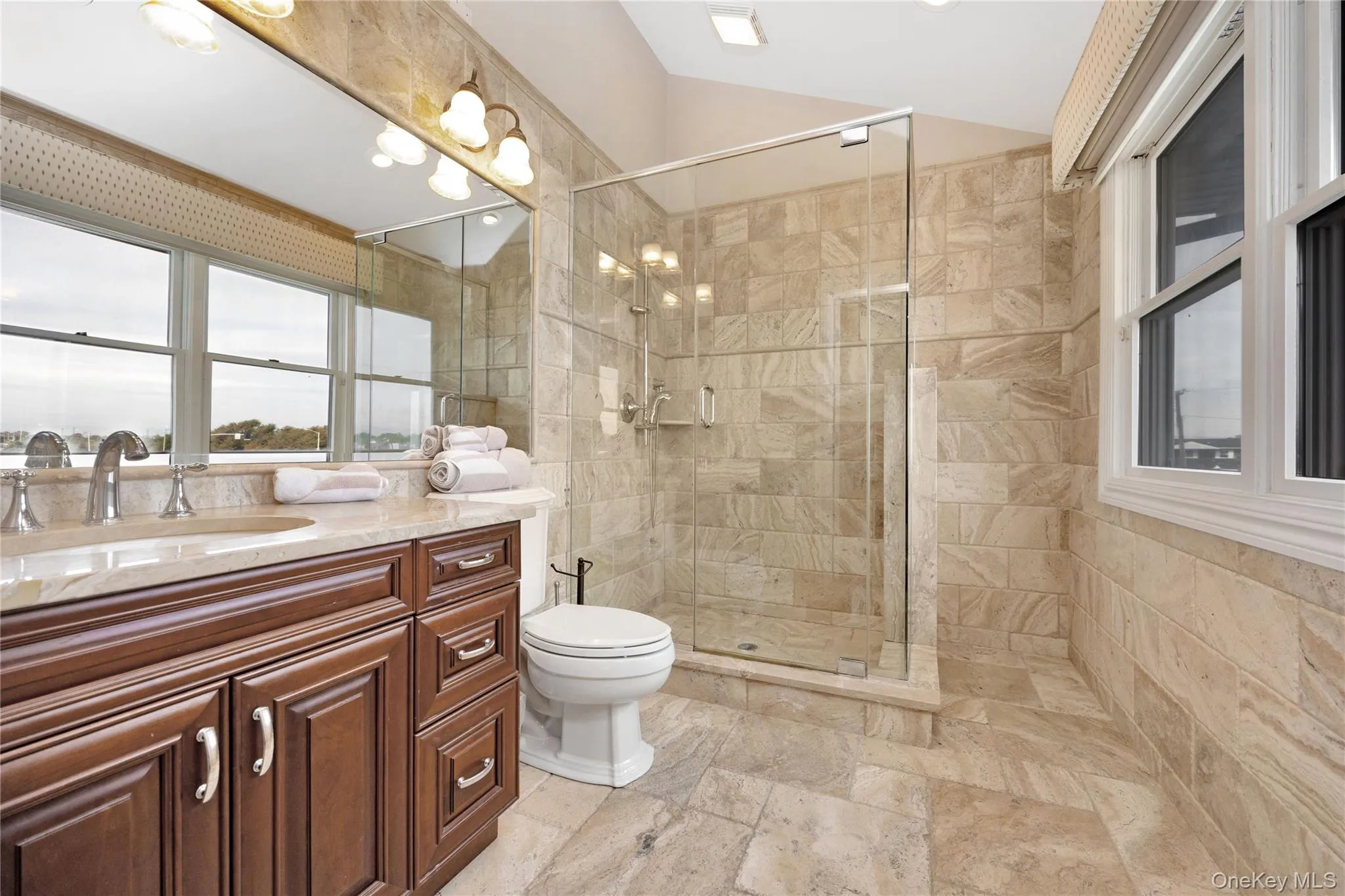 Bathroom with vanity, vaulted ceiling, a shower stall, and stone tile floors Bathroom with vanity, vaulted ceiling, a shower stall, and stone tile floors