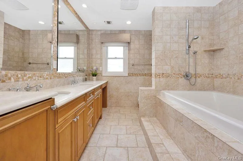 Bathroom featuring tile walls, double vanity, light tile patterned floors, tiled shower / bath, and recessed lighting Bathroom featuring tile walls, double vanity, light tile patterned floors, tiled shower / bath, and recessed lighting