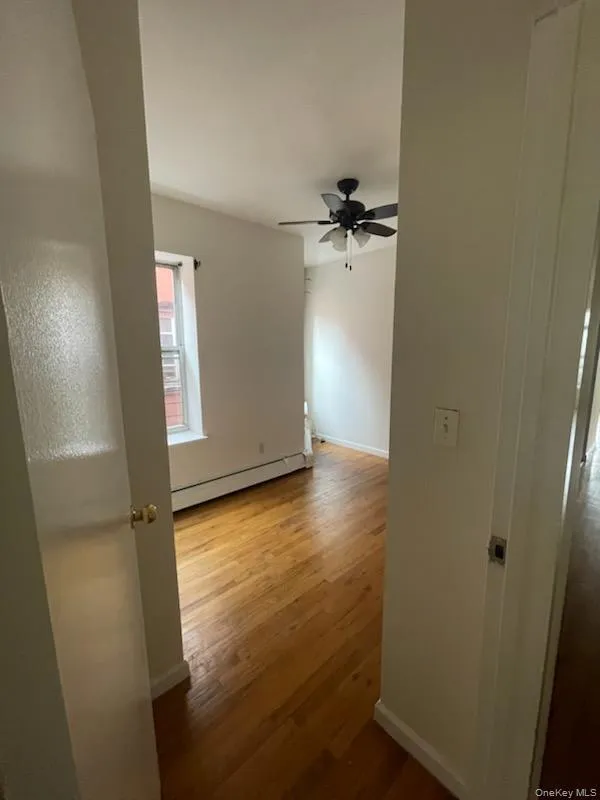 Spare room with baseboard heating, wood finished floors, and a ceiling fan Spare room with baseboard heating, wood finished floors, and a ceiling fan