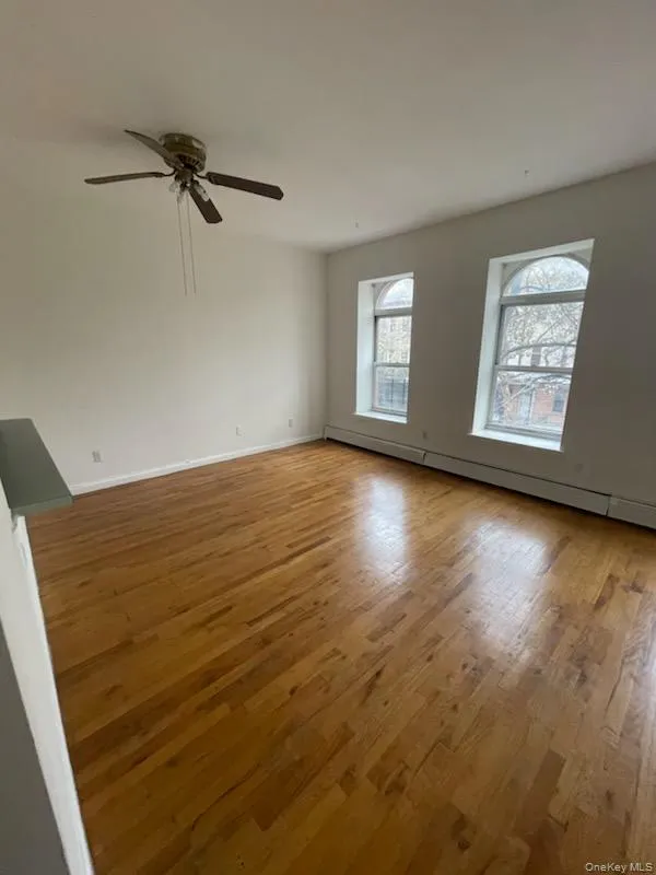 Empty room with baseboard heating, light wood finished floors, and a ceiling fan Empty room with baseboard heating, light wood finished floors, and a ceiling fan