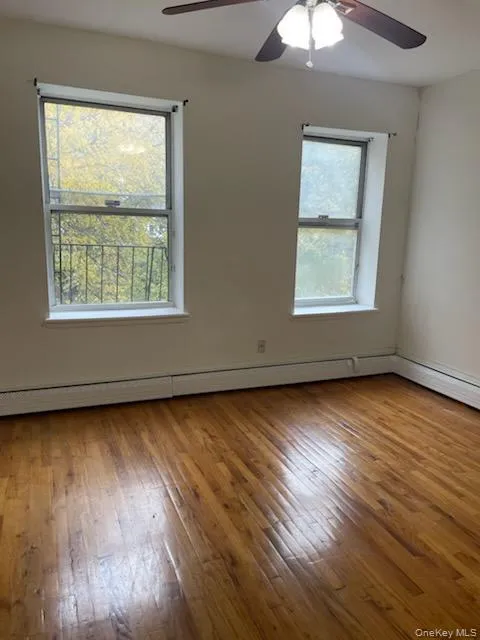 Empty room with light wood-style flooring, ceiling fan, and a baseboard heating unit Empty room with light wood-style flooring, ceiling fan, and a baseboard heating unit