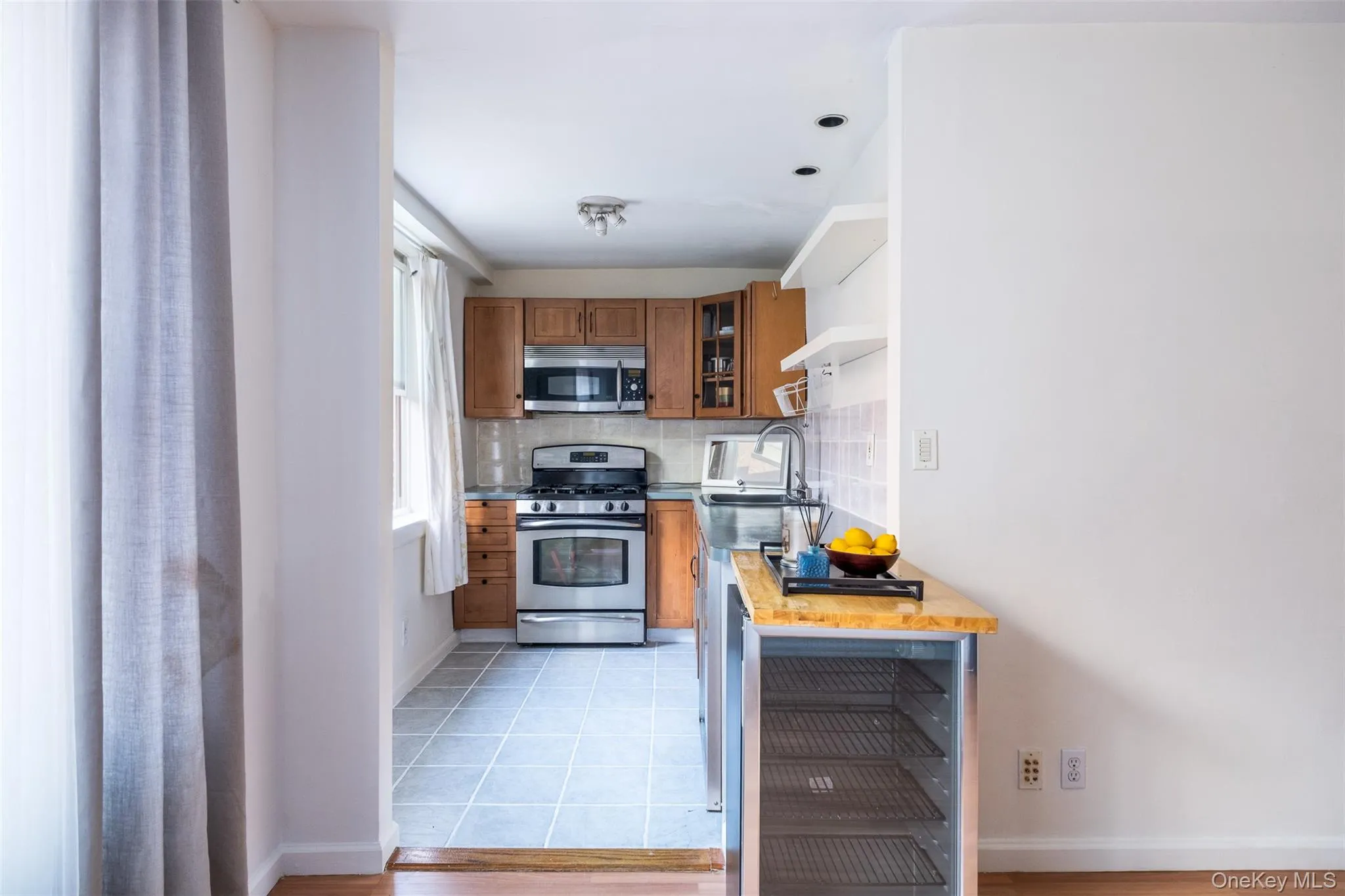 Kitchen with appliances with stainless steel finishes, wine cooler, decorative backsplash, brown cabinets, and glass insert cabinets Kitchen with appliances with stainless steel finishes, wine cooler, decorative backsplash, brown cabinets, and glass insert cabinets