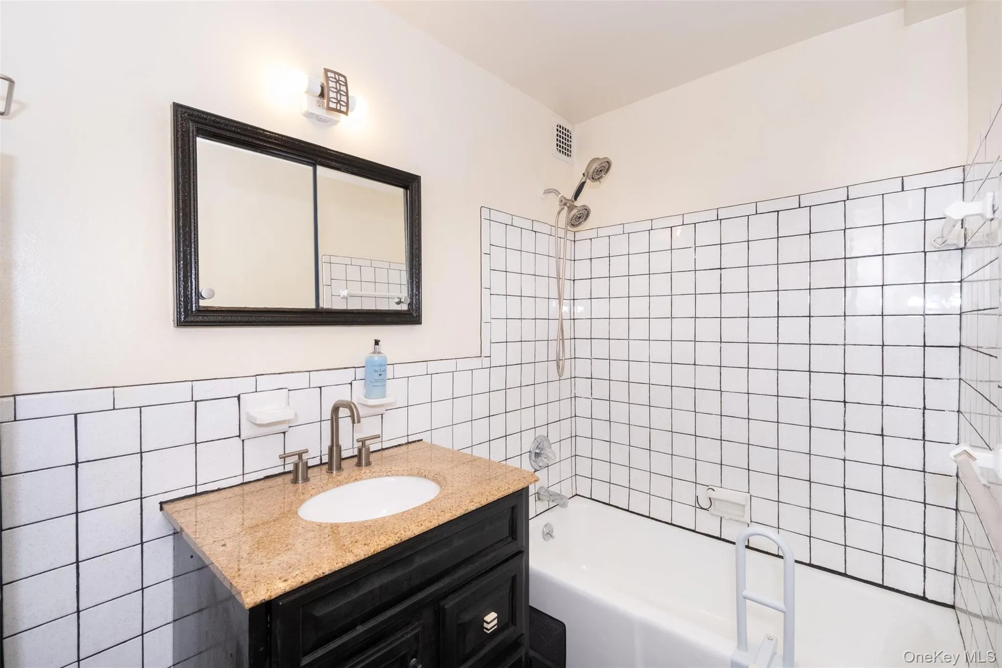 Full bathroom with tile walls, shower / bath combination, vanity, and a wainscoted wall Full bathroom with tile walls, shower / bath combination, vanity, and a wainscoted wall