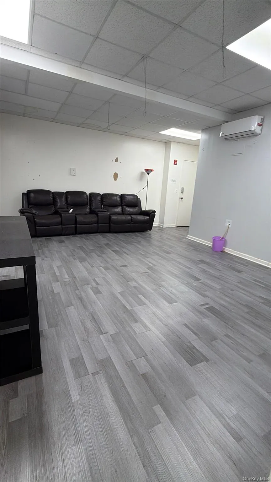 Finished below grade area with light wood-style floors, a paneled ceiling, and an AC wall unit Finished below grade area with light wood-style floors, a paneled ceiling, and an AC wall unit