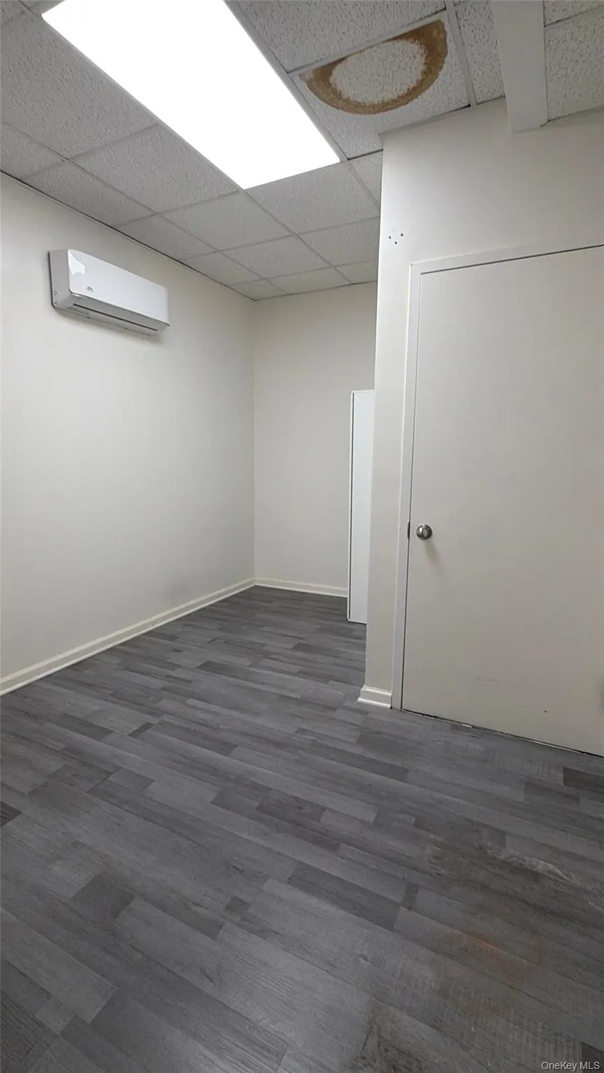 Empty room featuring dark wood-style floors, a drop ceiling, and a wall mounted AC Empty room featuring dark wood-style floors, a drop ceiling, and a wall mounted AC